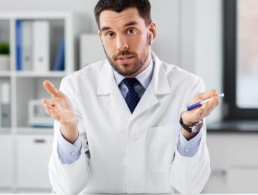 doctor-earphones-having-video-call-clinic healthcare, medicine and people concept - male doctor with earphones having video conference at hospital